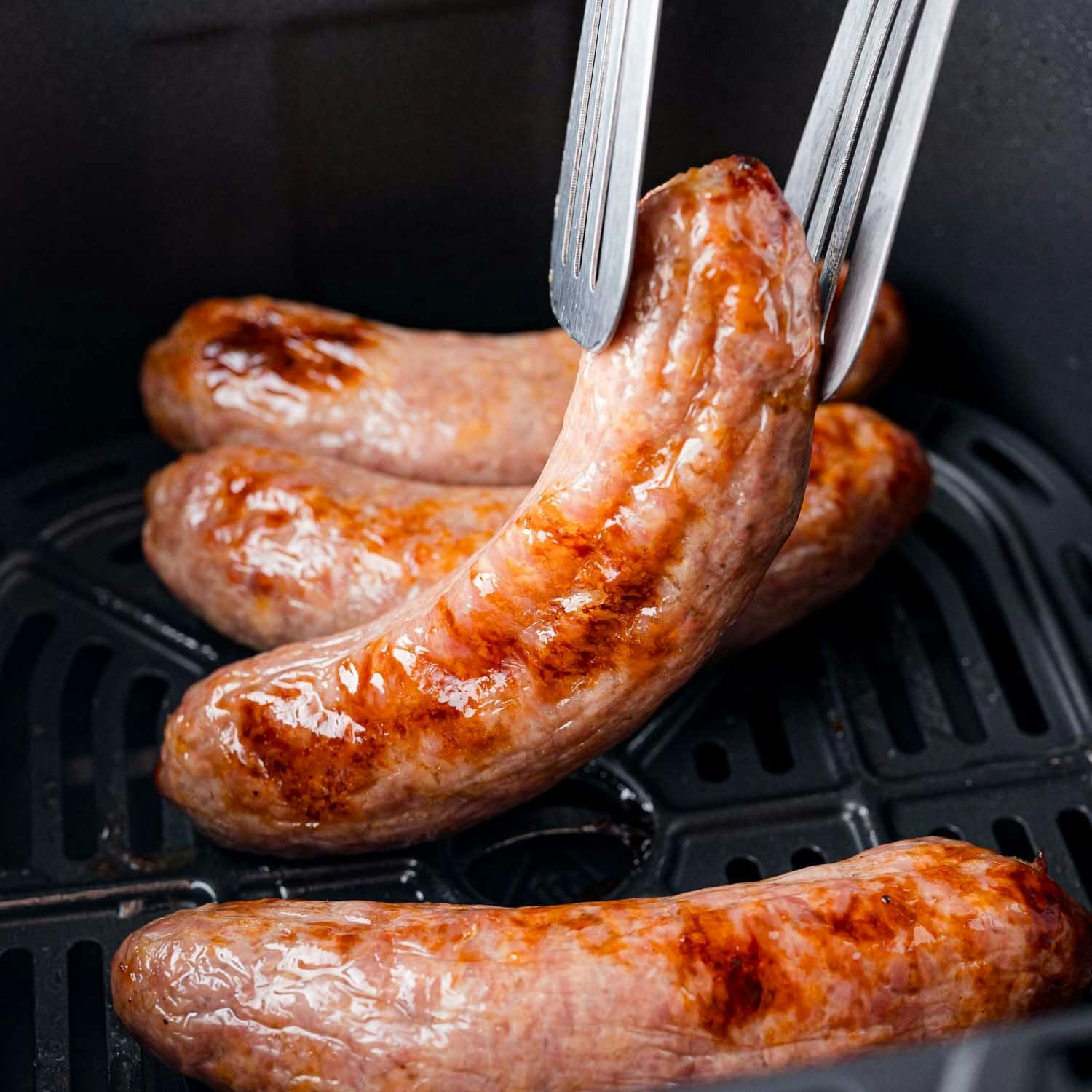 Air fryer brat held with tongs.