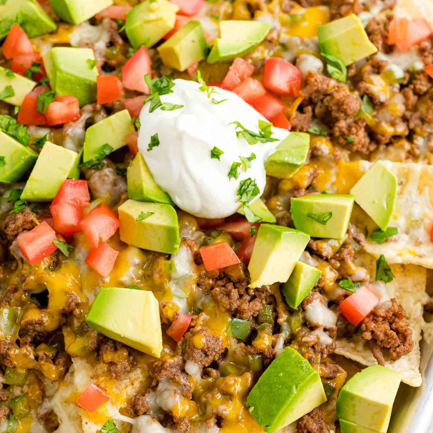 Beef nachos topped with avocado, tomato, sour cream, cilantro.