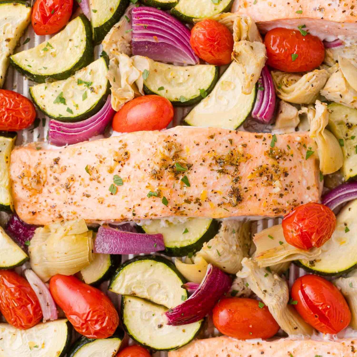 Salmon with Greek seasonings, on a sheet pan with tomatoes, zucchini, red onions, and artichoke hearts.