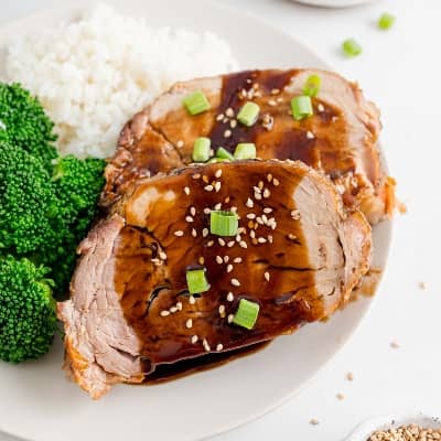 Two slices of pork loin with a thick balsamic glaze and sesame seeds and green onions.