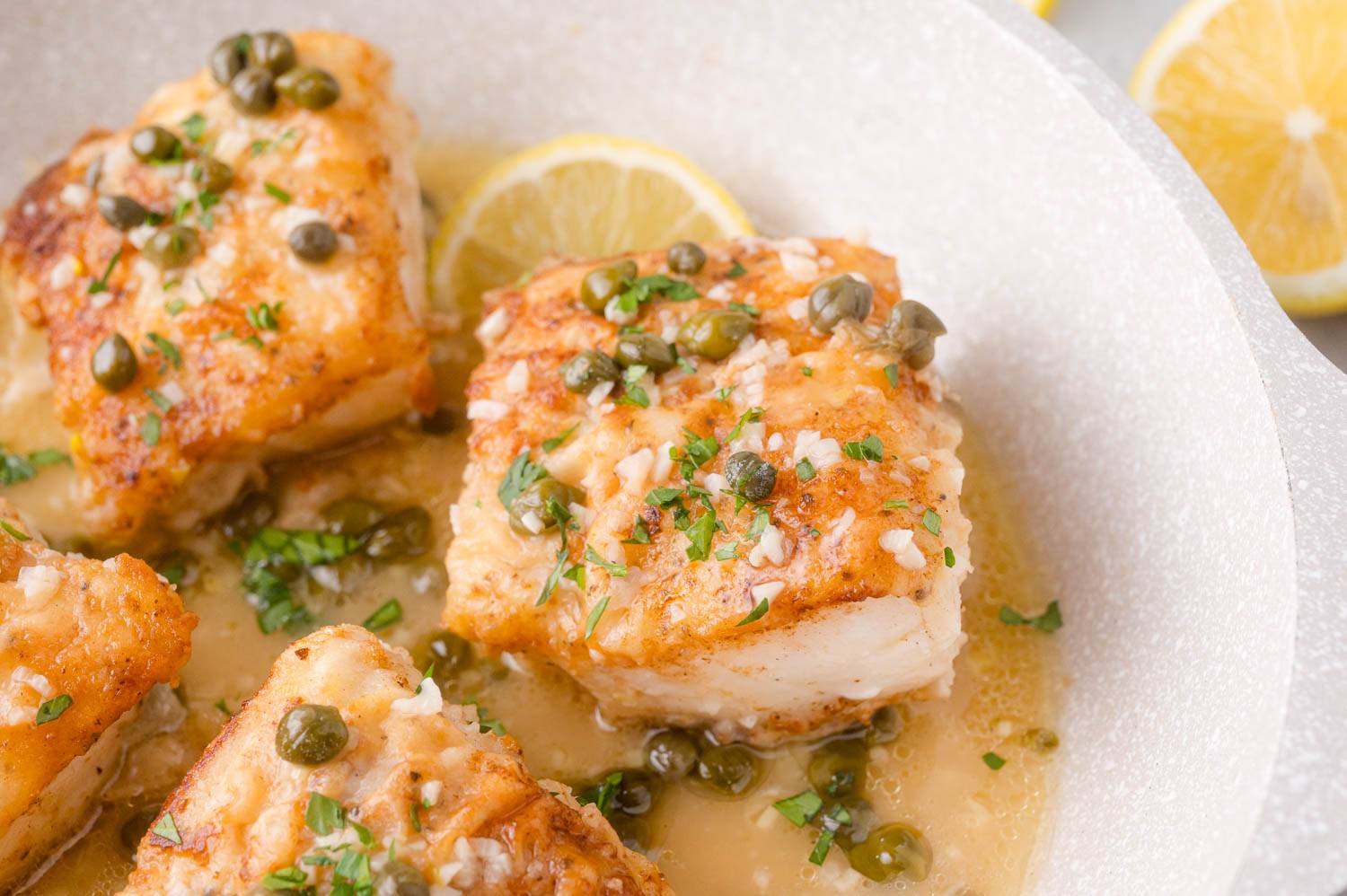 Cod piccata in a pan, topped with capers, garlic, and fresh parsley.
