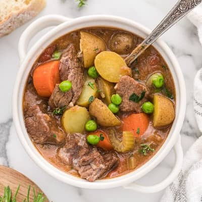 Crockpot beef stew in a small white bowl with two handles.