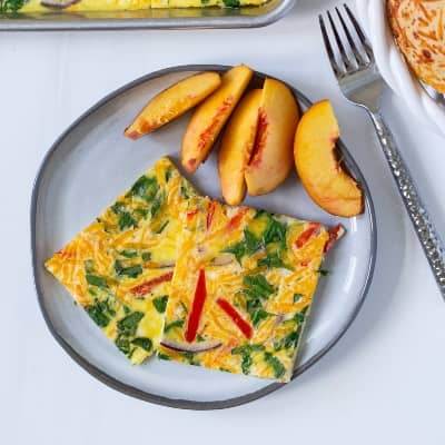 Two slices of sheet pan eggs on a plate with sliced peaches.