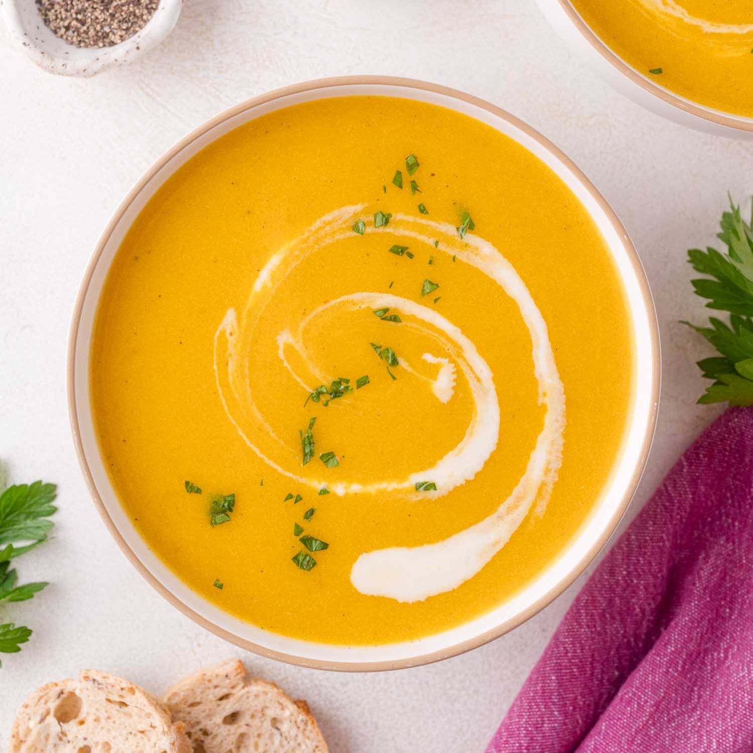 Kabocha squash soup in a white bowl with a swirl of cream and a sprinkle of parsley.