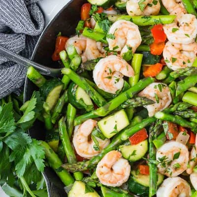 Shrimp and fresh spring vegetables in a black skillet.