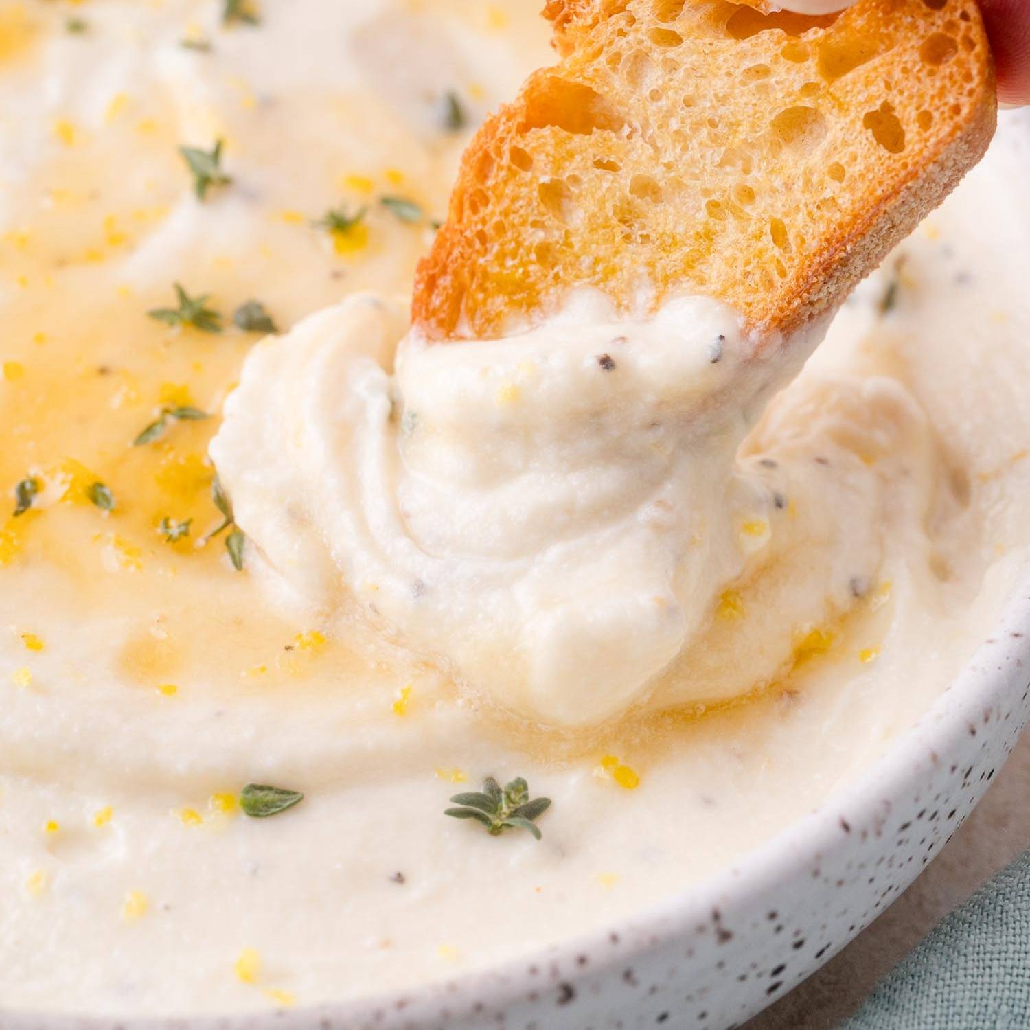 Whipped ricotta toppped with honey and fresh thyme, with a slice of bread being dipped into it.
