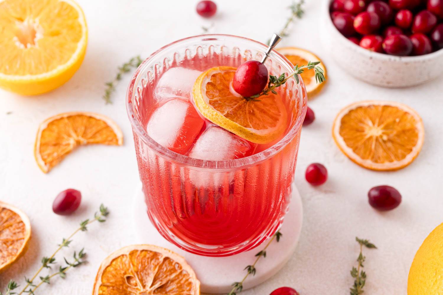 Cranberry thyme spritzer in a short glass garnished with a dehydrated orange and cranberries.