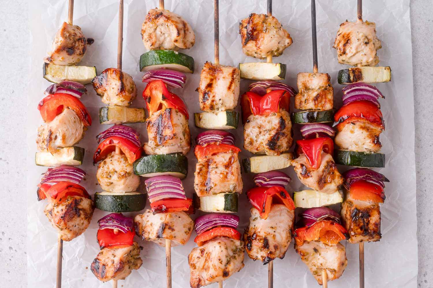 Chicken kabobs lined up on parchment paper.