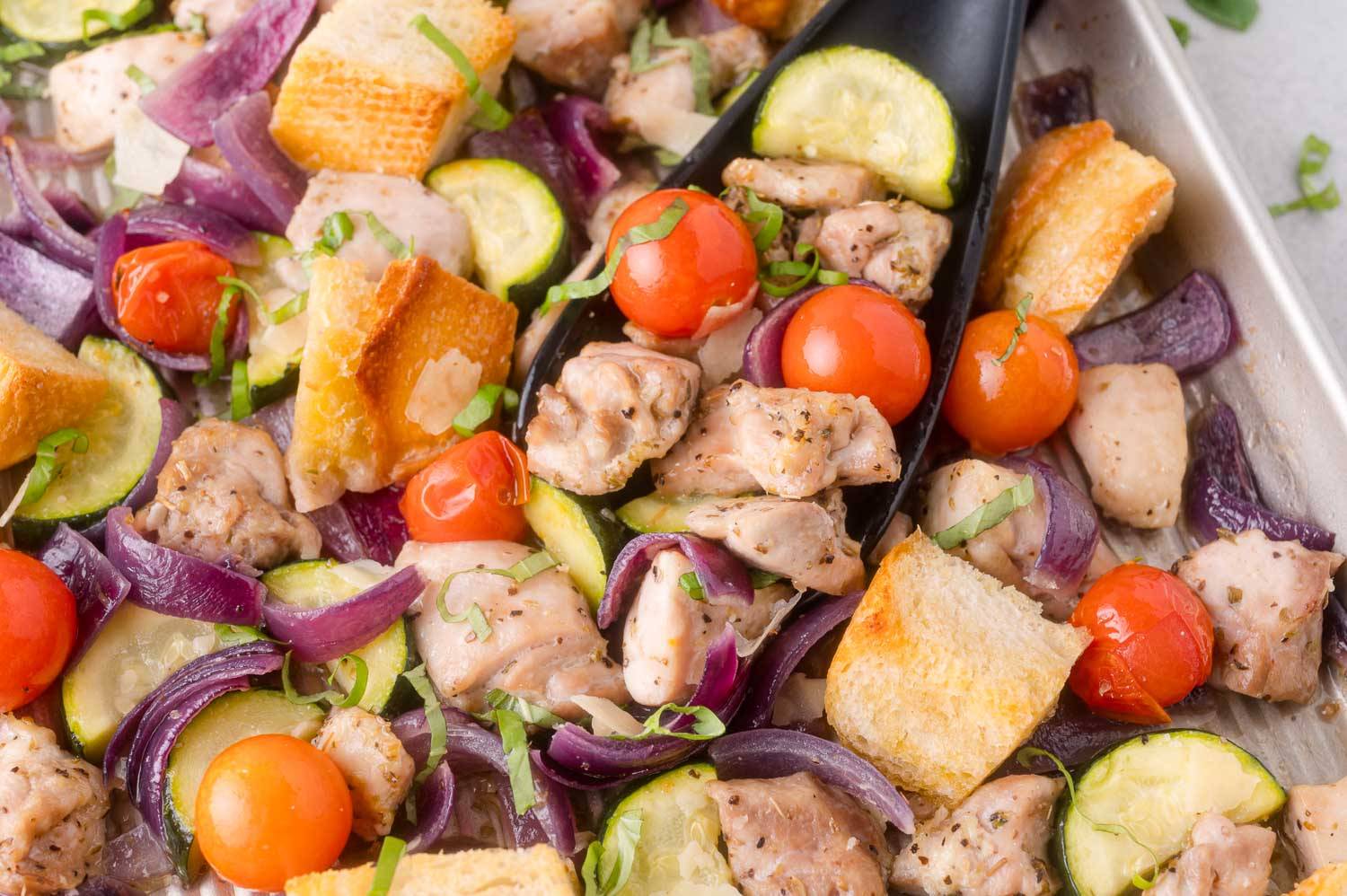 Sheet pan dinner with chicken, tomatoes, bread cubes, zucchini, and fresh herbs.