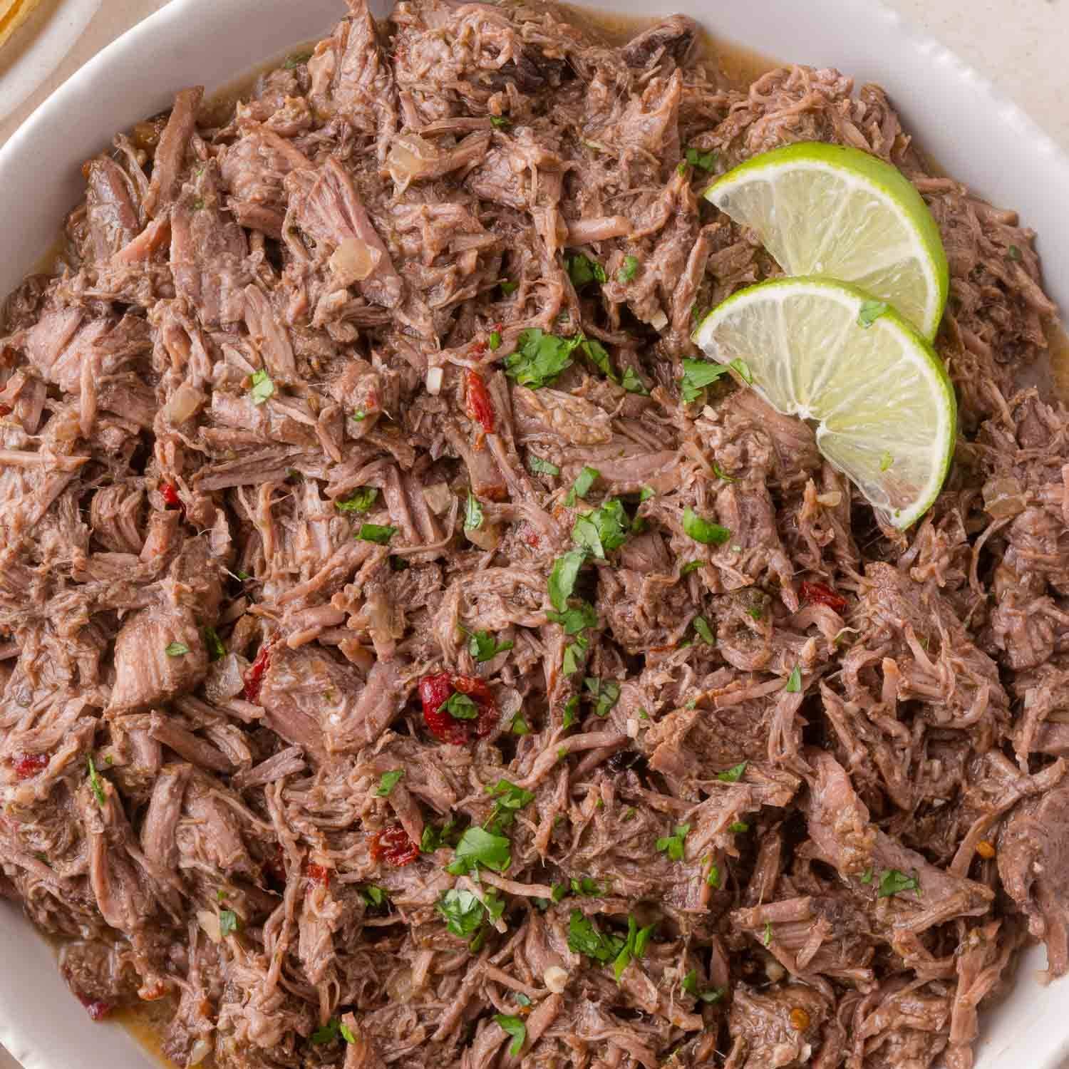 Shredded beef barbacoa in a bowl, topped with two lime slices.