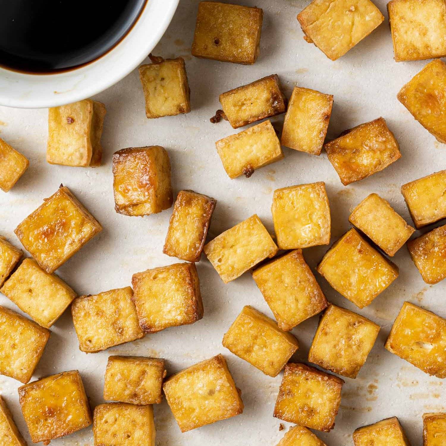 Baked tofu on a white surface with dark brown sauce in the upper right hand corner.
