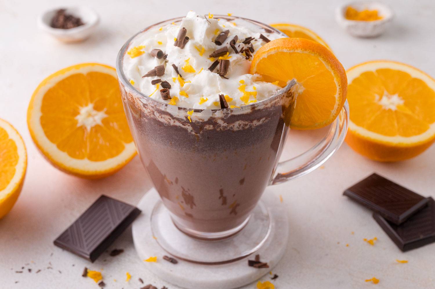 Orange hot chocolate in a clear mug, topped with whipped cream, shaved chocolate, and orange zest.