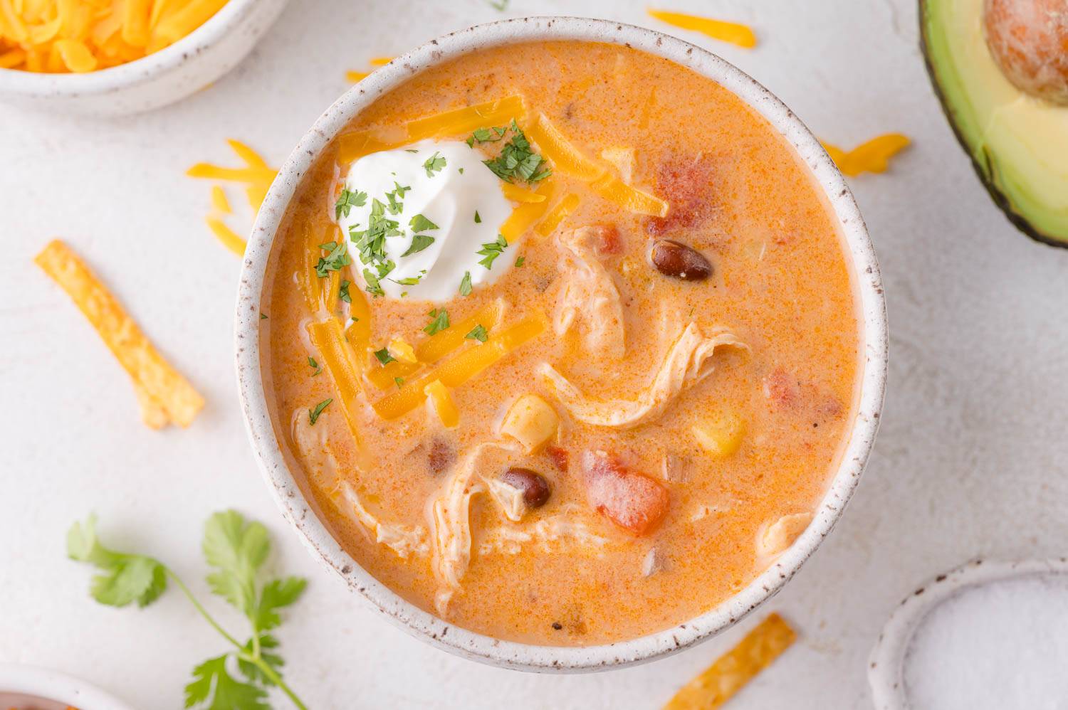 Chicken enchilada soup in a small bowl, topped with cheddar cheese, sour cream, and cilantro.