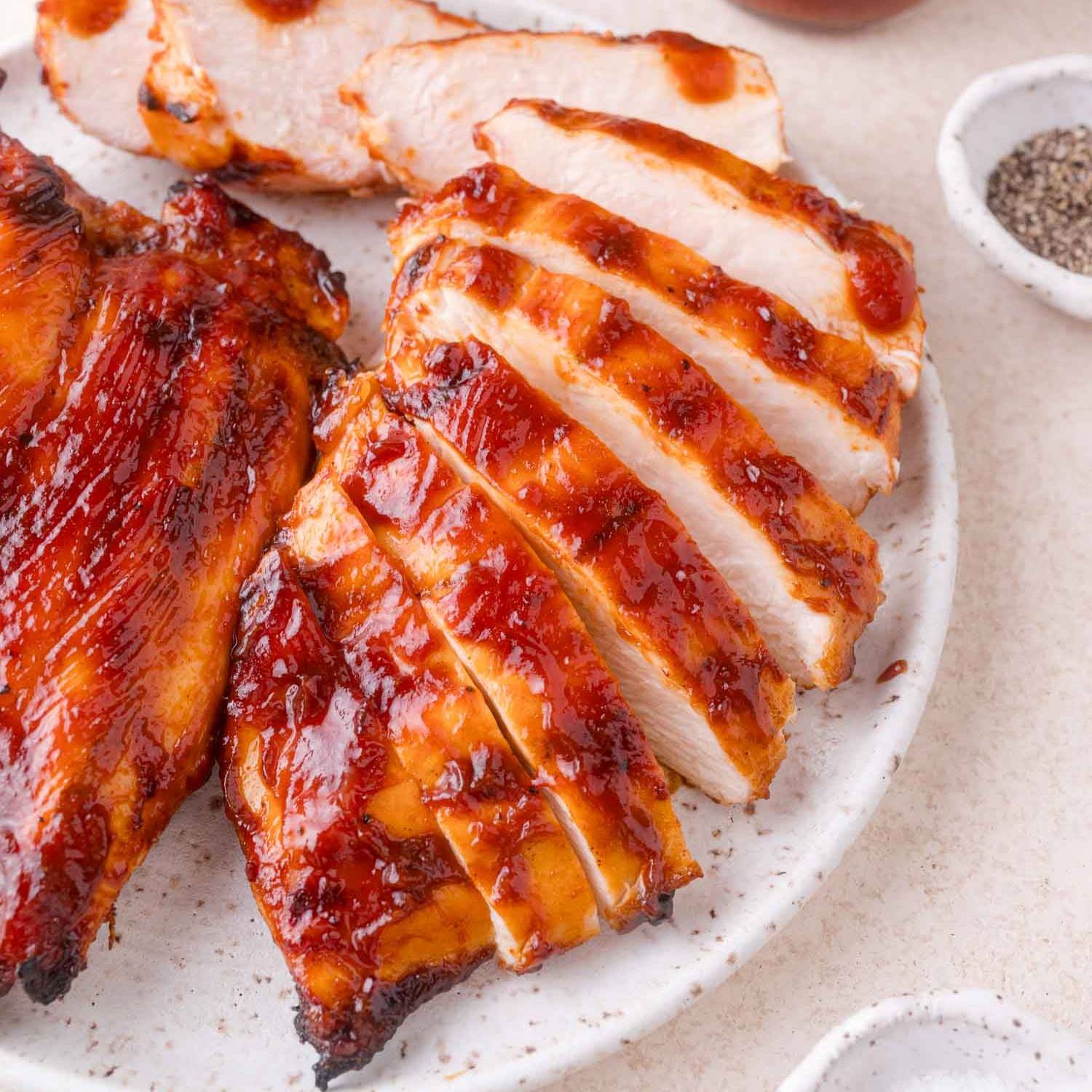 Sliced barbecued chicken breast on a plate with others.