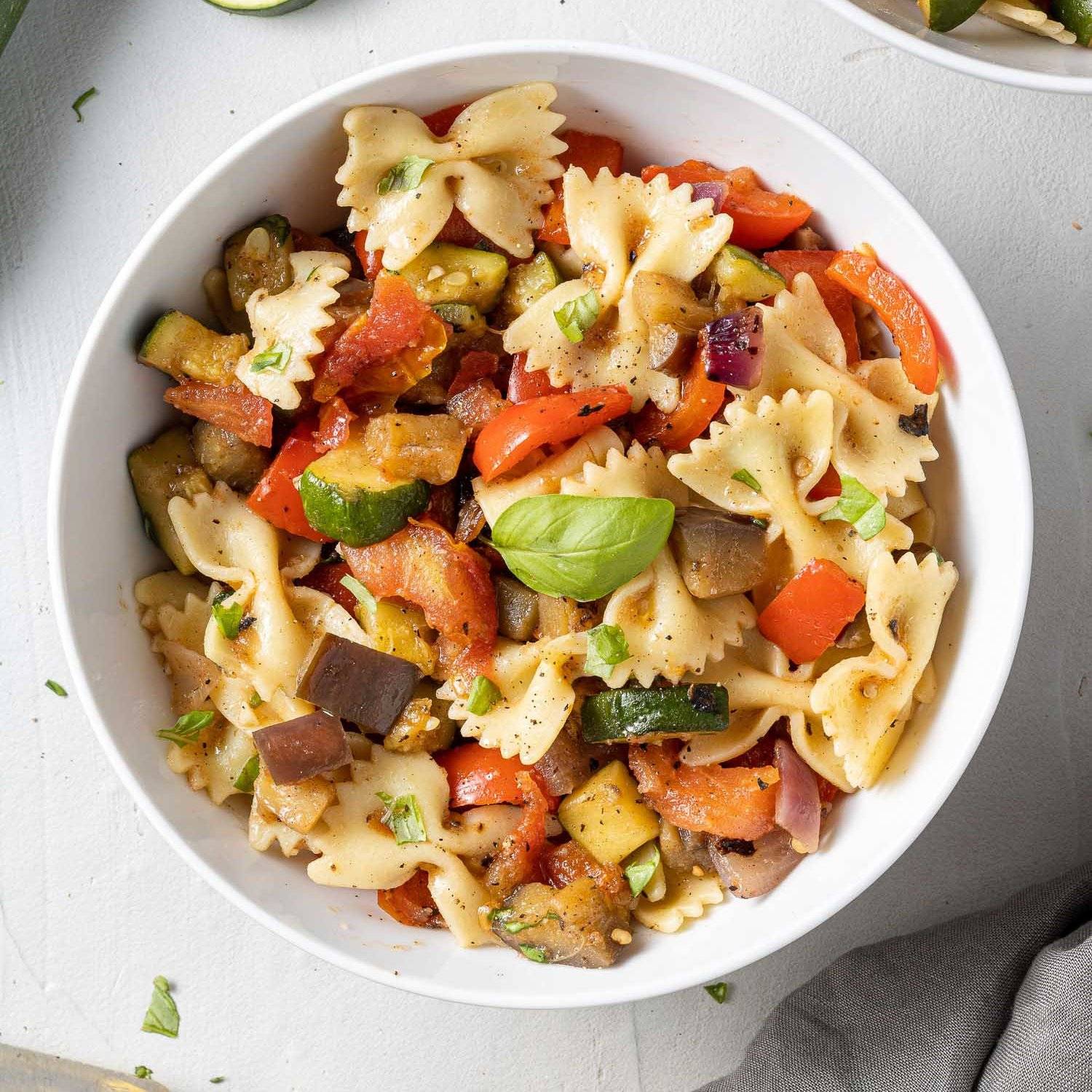 Grilled vegetables and basil in a bowl with bowtie pasta.