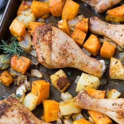Chicken drumstick, potatoes, and sweet potatoes on a sheet pan.