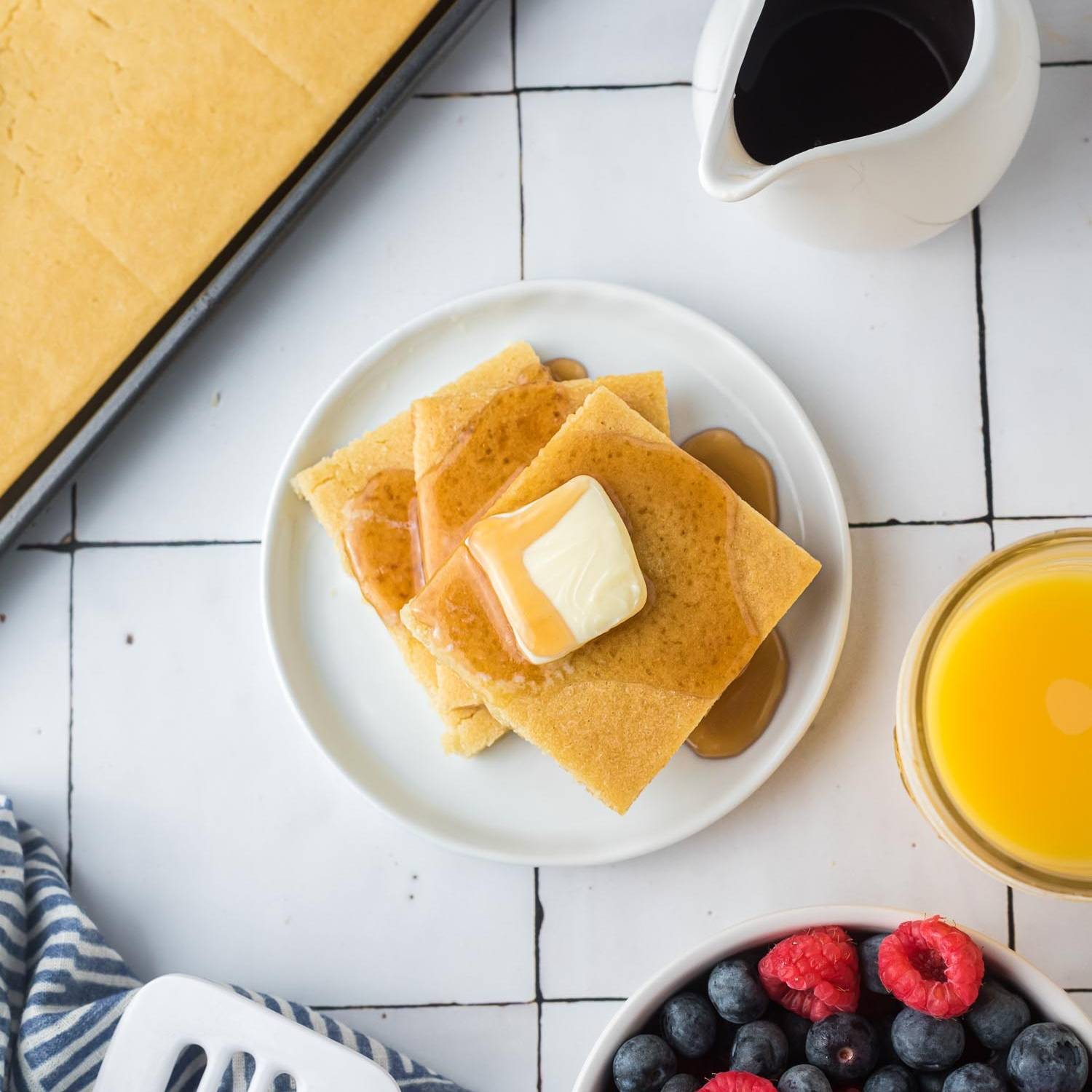 Square pancakes on a plate, topped with butter and maple syrup.