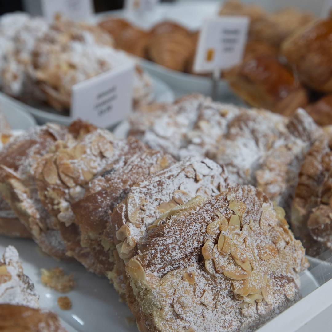 A bakery display of almond-topped pastries dusted with icing sugar.