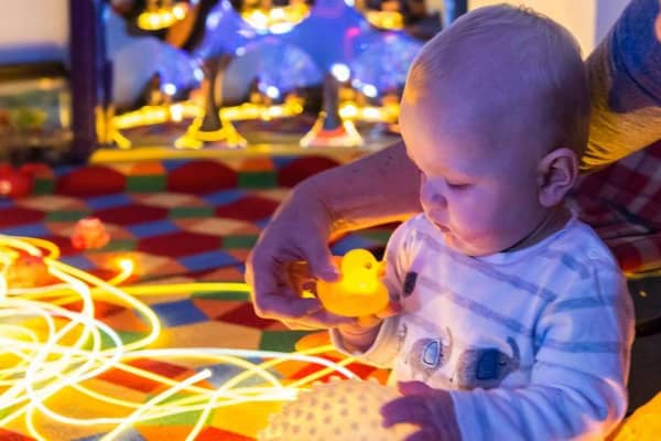 A baby plays with a small yellow rubber duck while exploring a glowing sensory play setup with fibre optic lights.