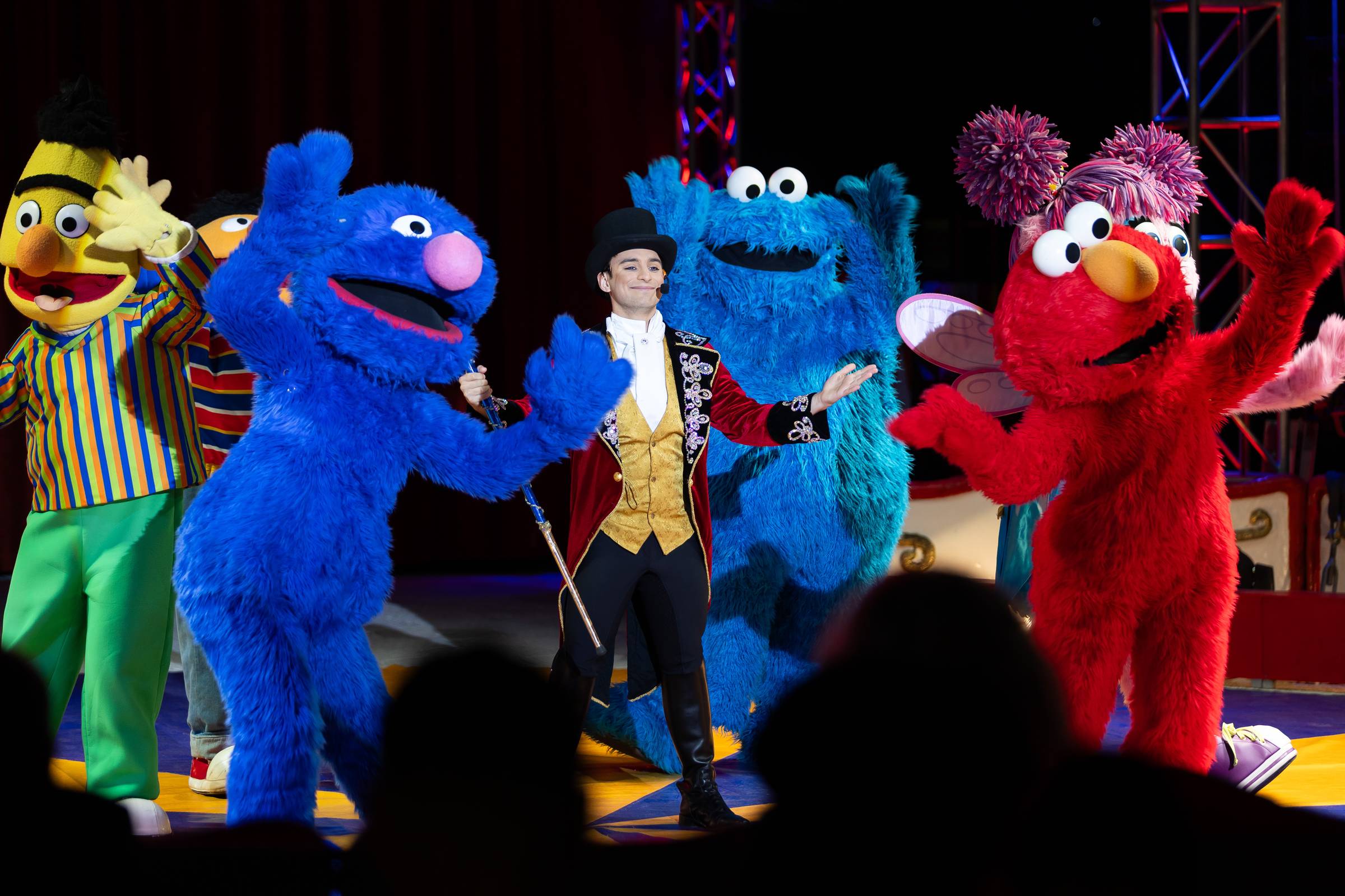 Sesame Street characters including Bert, Grover, Cookie Monster, Elmo and Abby on stage with a ringmaster during a circus performance.