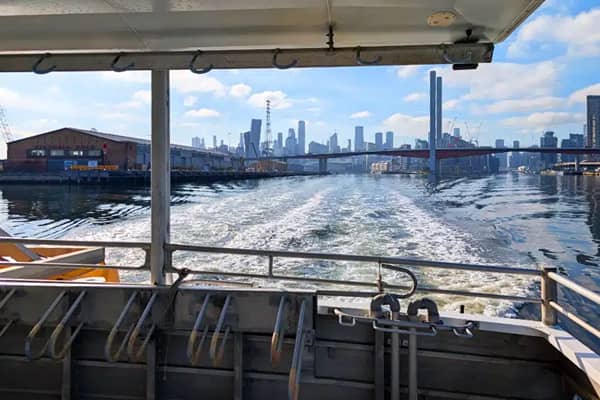View from the back deck of a ferry looking out over its wake toward the Melbourne city skyline and a bridge in the distance