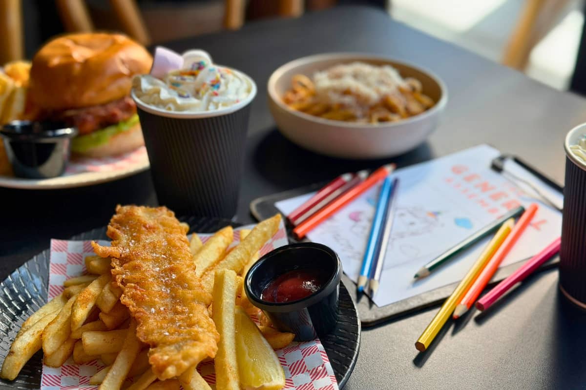 A kids' meal of fish and chips, a burger, curly fries and a hot chocolate topped with marshmallows, alongside a colouring sheet and pencils at The General Assembly.