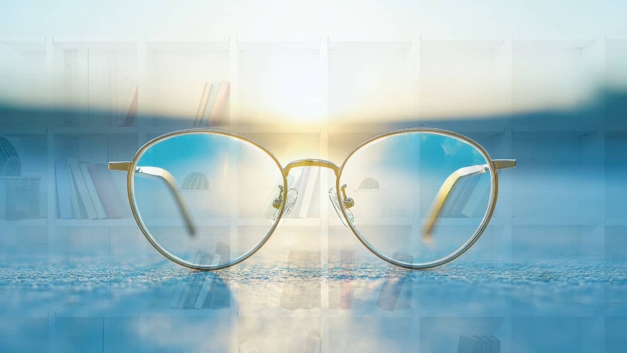 A set of glasses in front of a bookcase, lit up by the sunrise