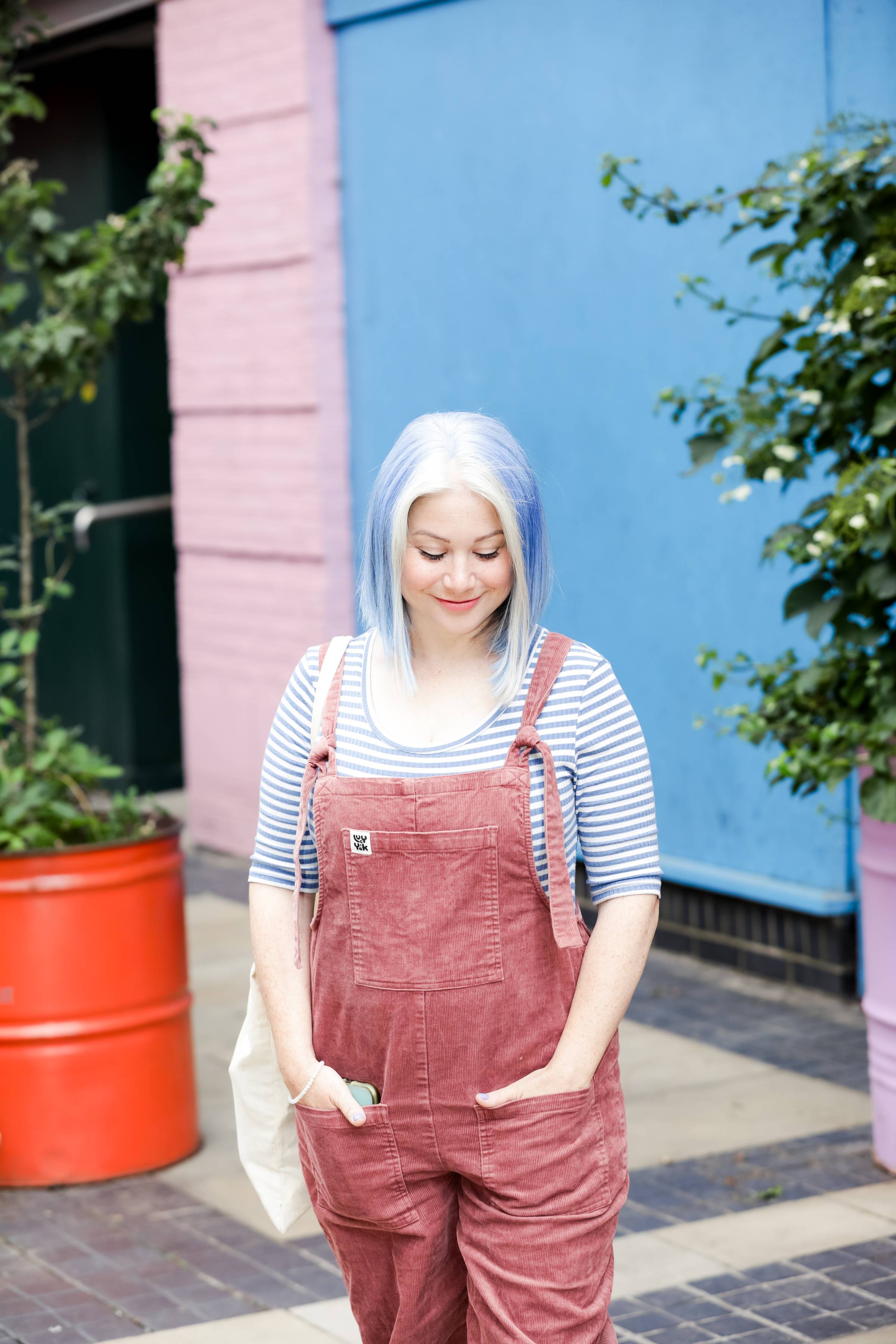 Laila looks down to the floor, dresses in dungarees and stripy tshirt