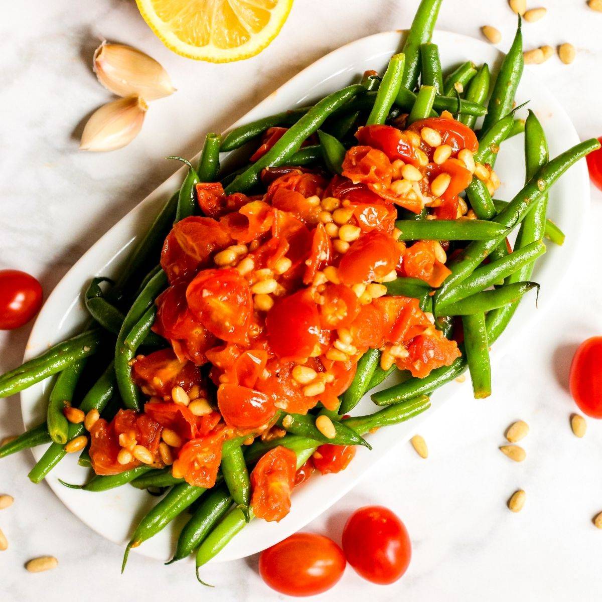 Platter of green beans topped with sauteed tomatoes and pine nuts.
