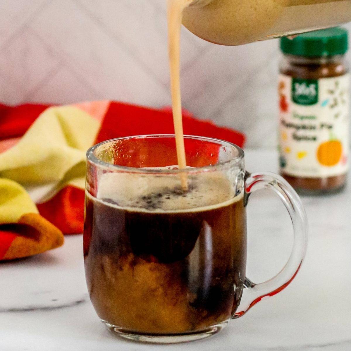 Pumpkin spice creamer being poured into a cup of coffee.