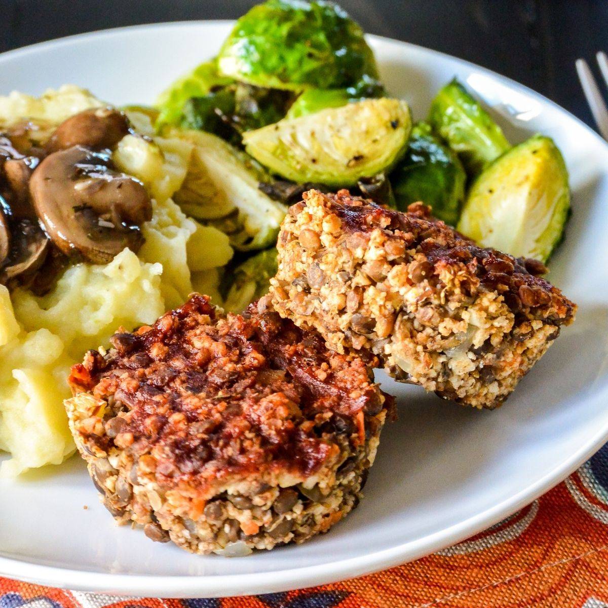 Dinner plate with lentil meatloaf muffins, mashed potatoes and gravy, and roasted Brussels sprouts.