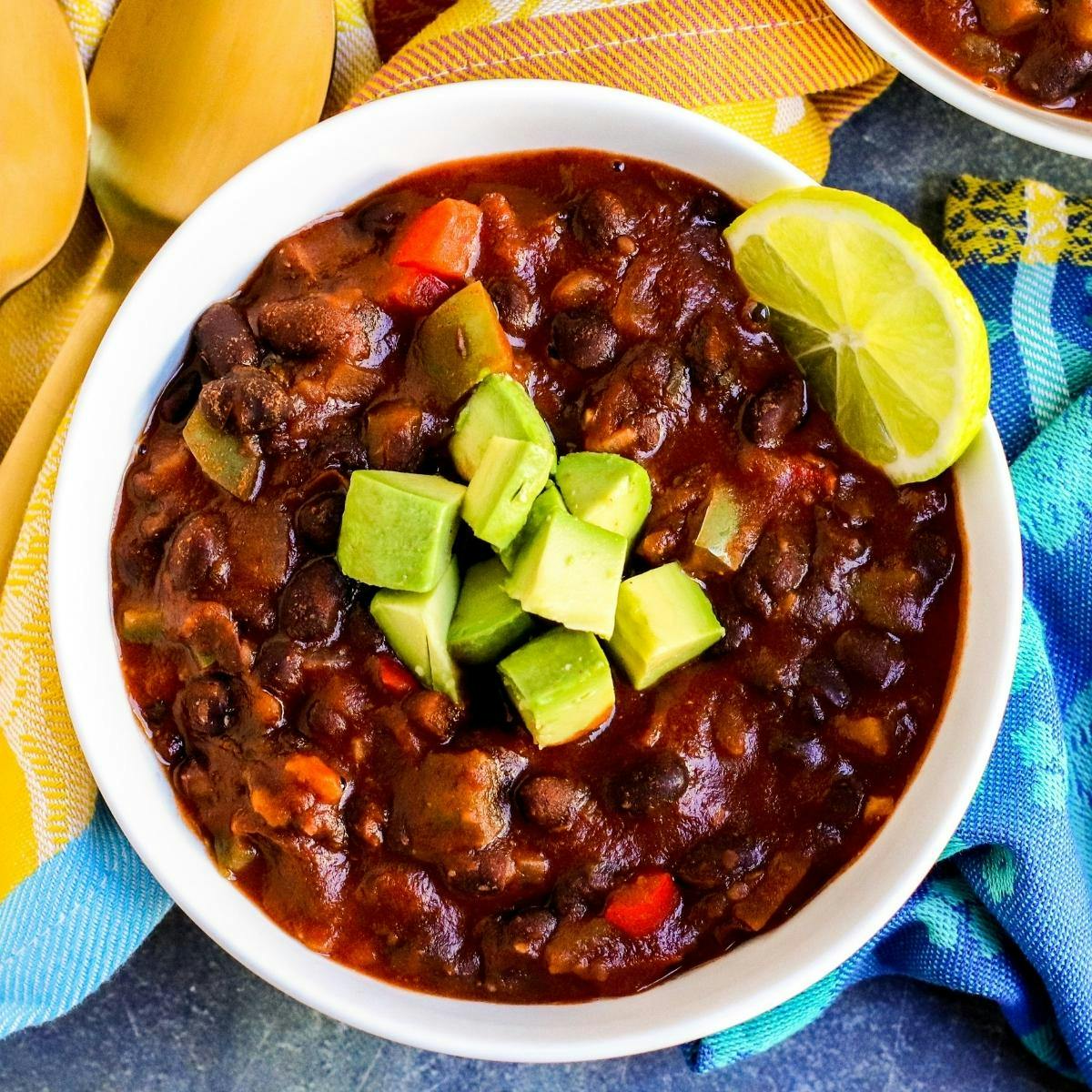 Bowl of black bean chili with a lime slice and cubed avocado.