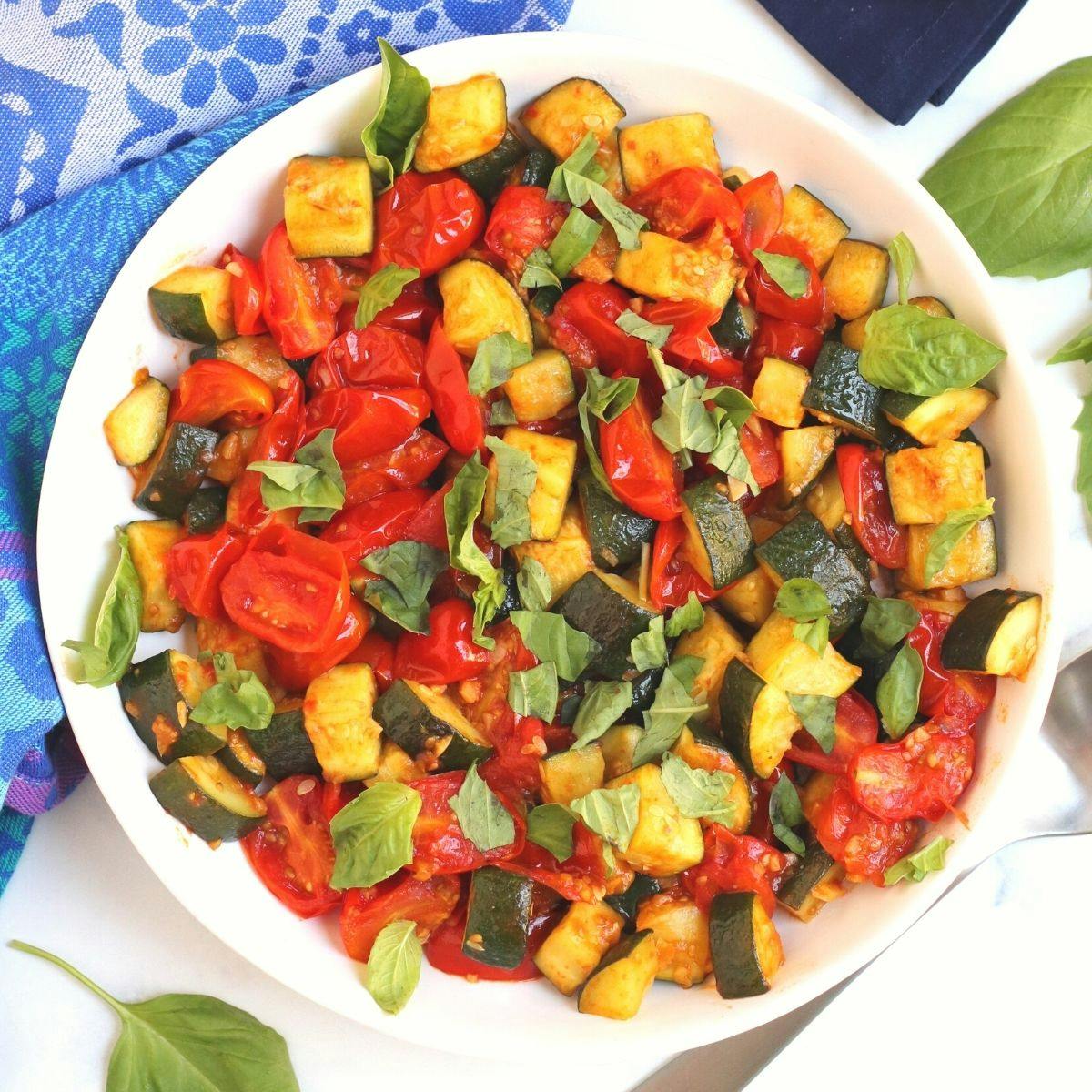 Bowl of Mediterranean tomato and zucchini saute garnished with fresh basil.