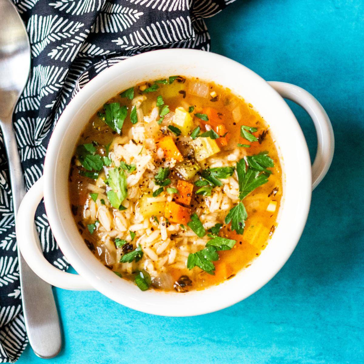 Bowl of vegetable rice soup garnished with parsley.