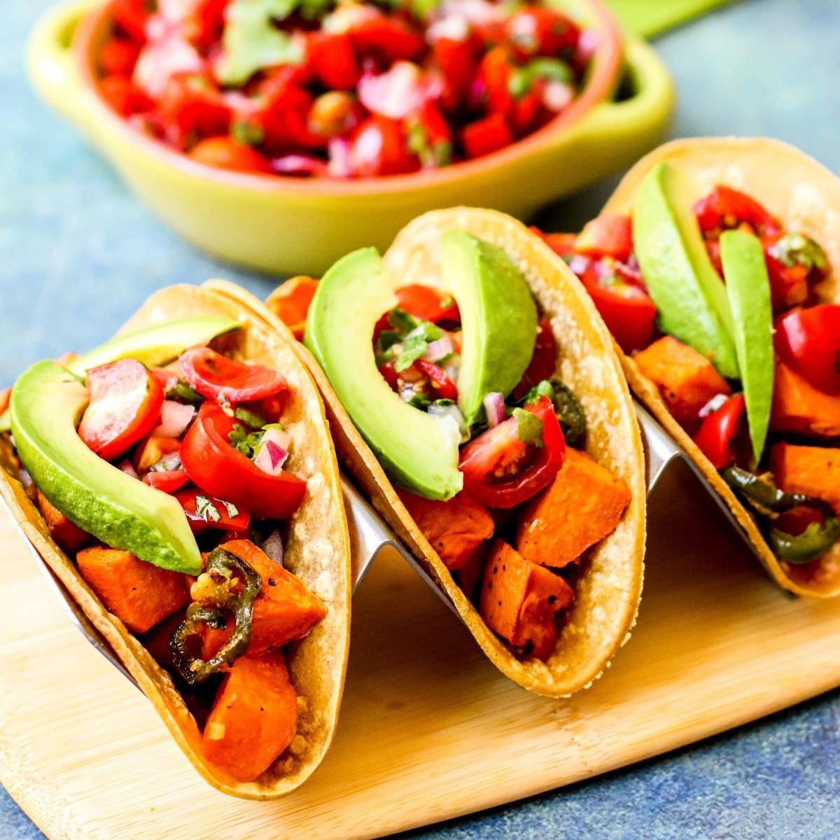 Roasted sweet potato tacos topped with cherry tomato salad and avocado slices.