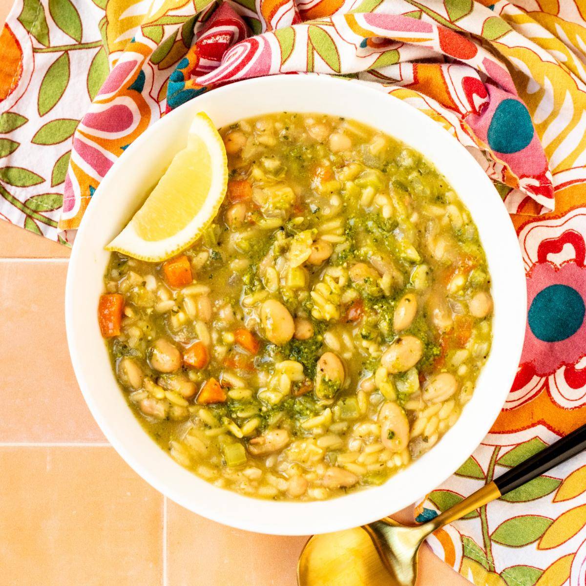 Bowl of pesto orzo soup with a lemon wedge.