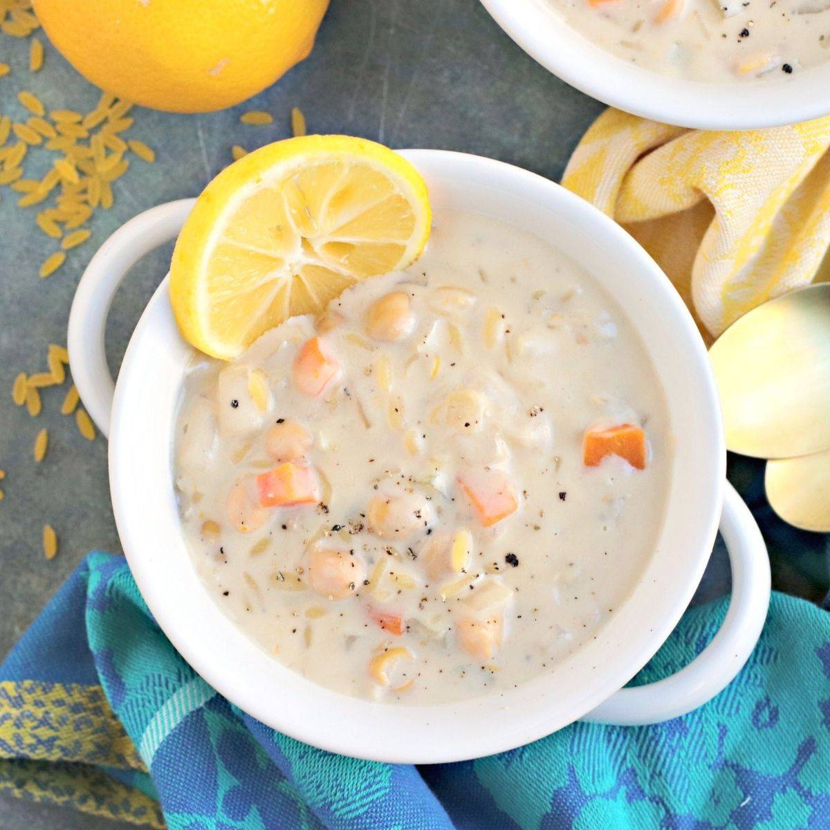 Bowl of creamy chickpea orzo soup with lemon slice on the side.