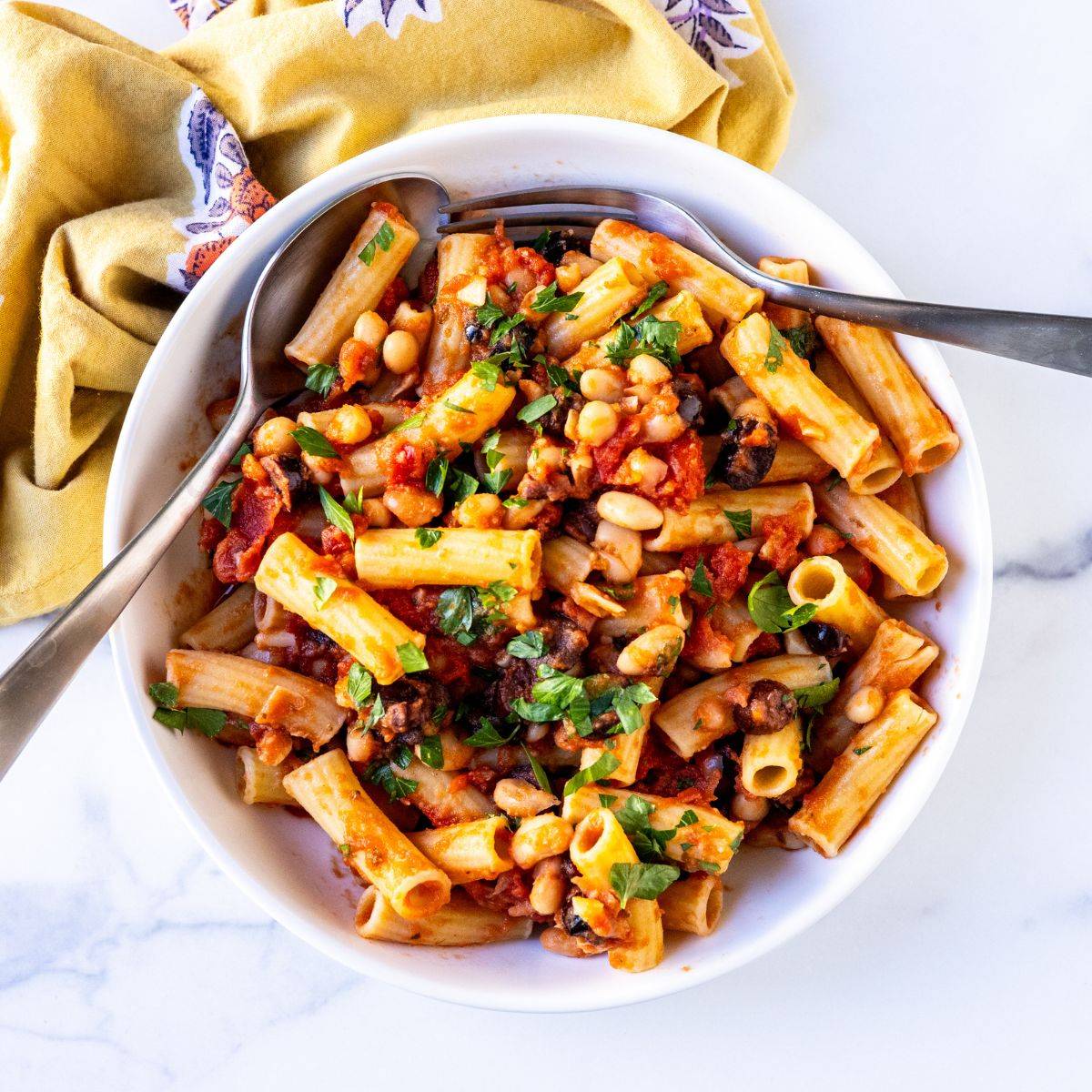 Bowl of rigatoni with white bean tomato sauce with Kalamata olives and parsley.