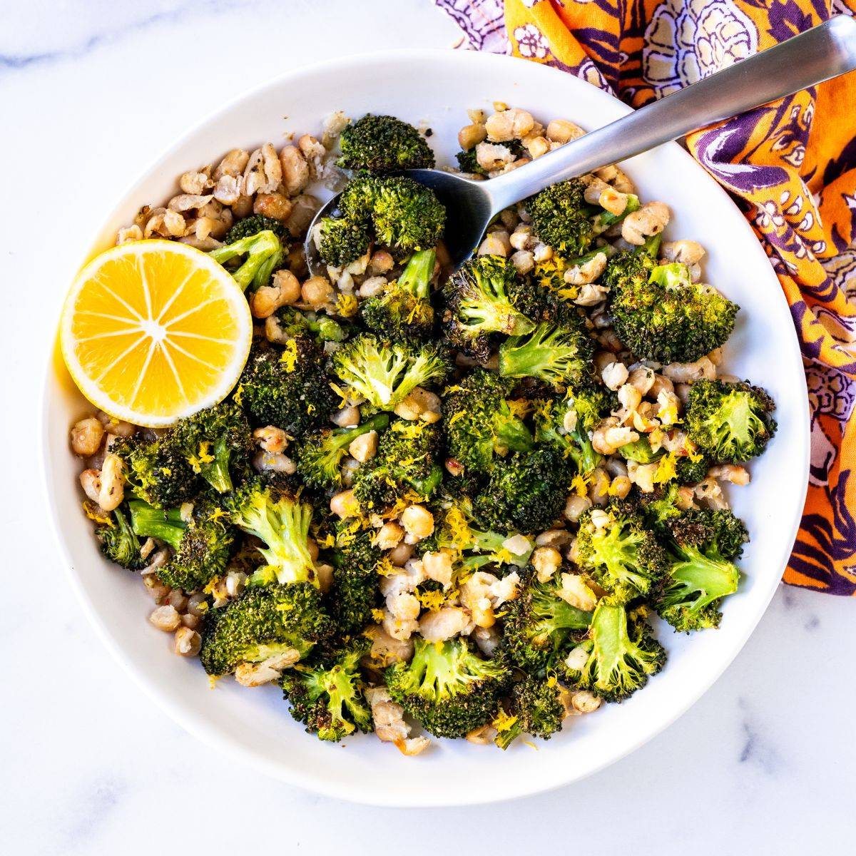 Roasted broccoli and white beans garnished with lemon zest and a slice of lemon.