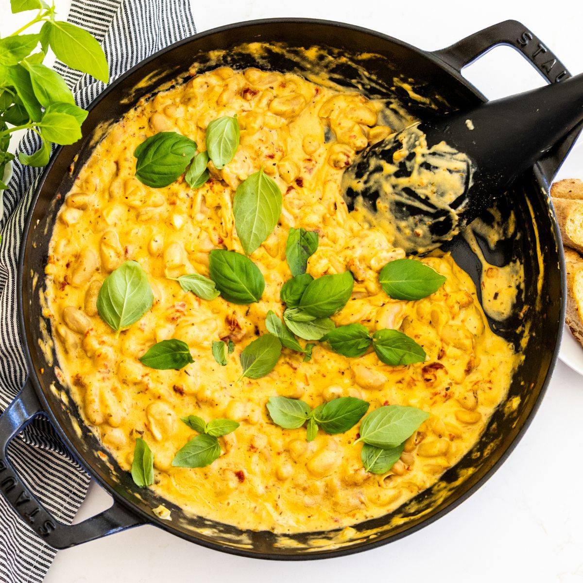 Creamy white bean skillet with sun-dried tomatoes garnished with fresh basil.