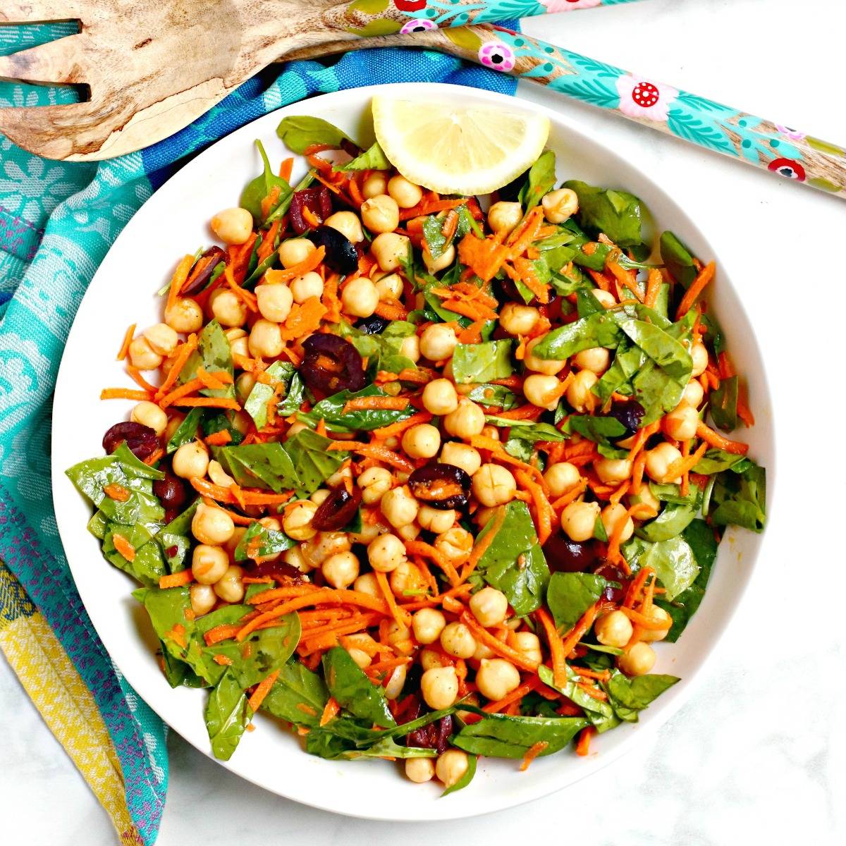 Bowl of spinach salad with chickpeas, carrots, and olives.