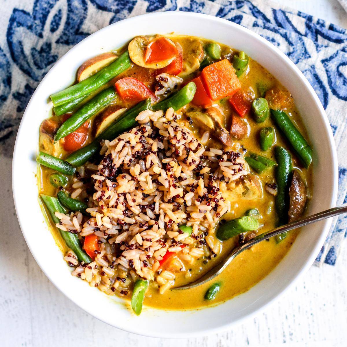 Bowl of green bean curry with brown rice and quinoa scooped on top.