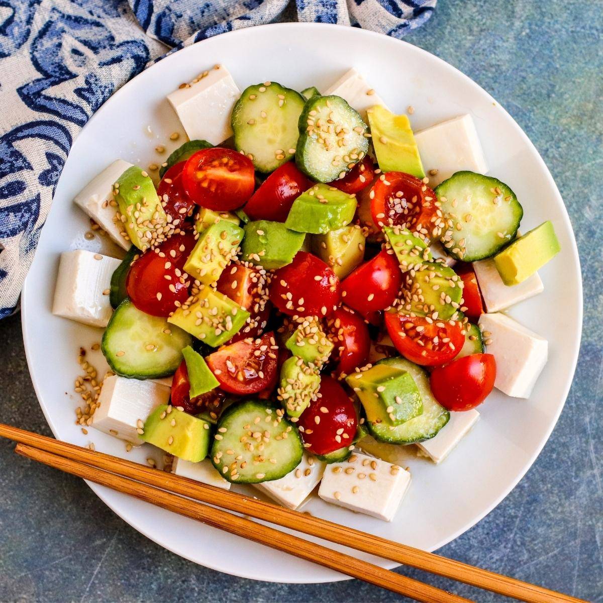Silken tofu salad with avocado, tomatoes, and cucumbers on a plate with chopsticks.