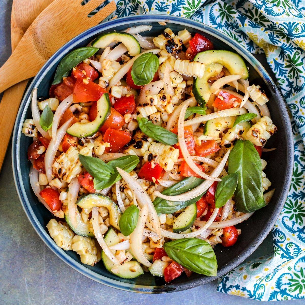 Bowl of grilled corn salad with tomatoes, cucumbers, onions, and basil.