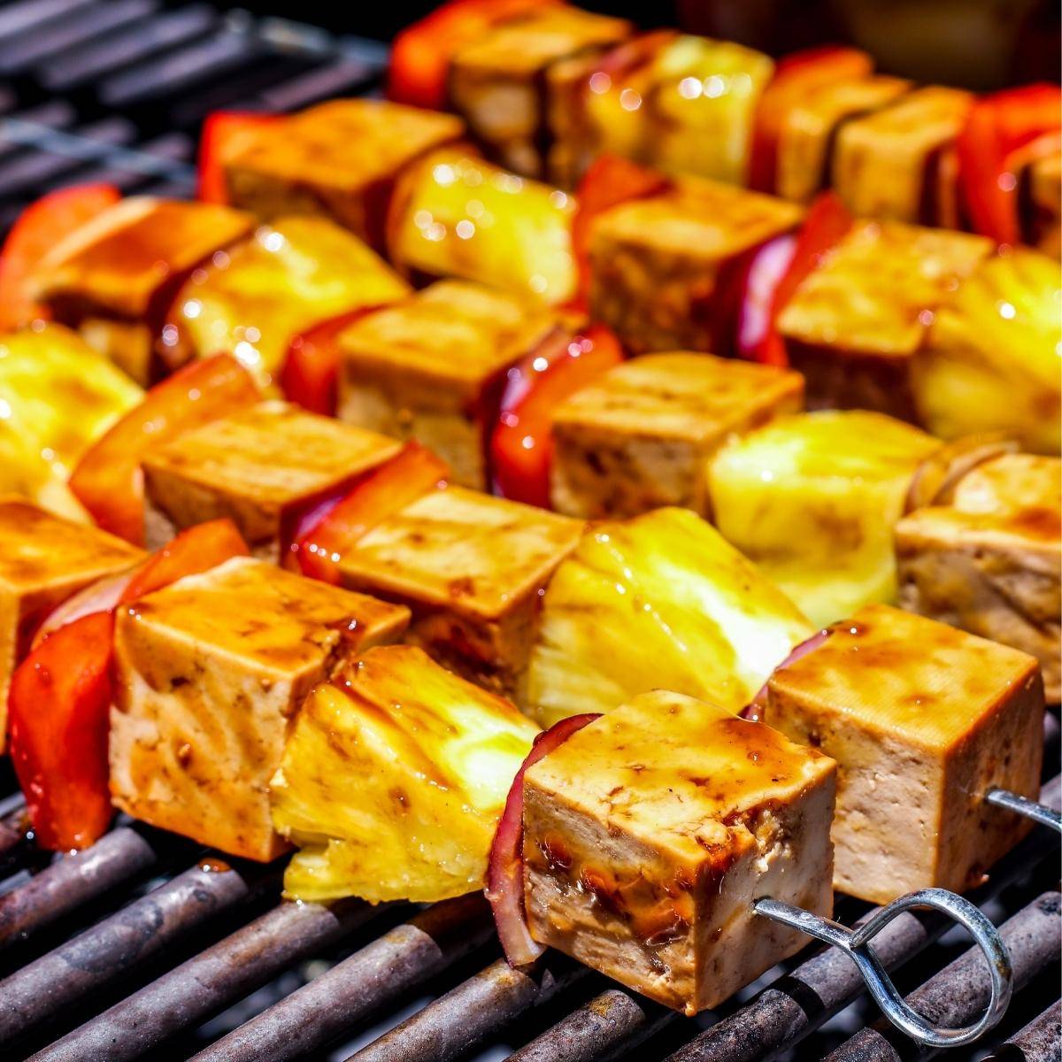 Pineapple and tofu teriyaki skewers on a grill.