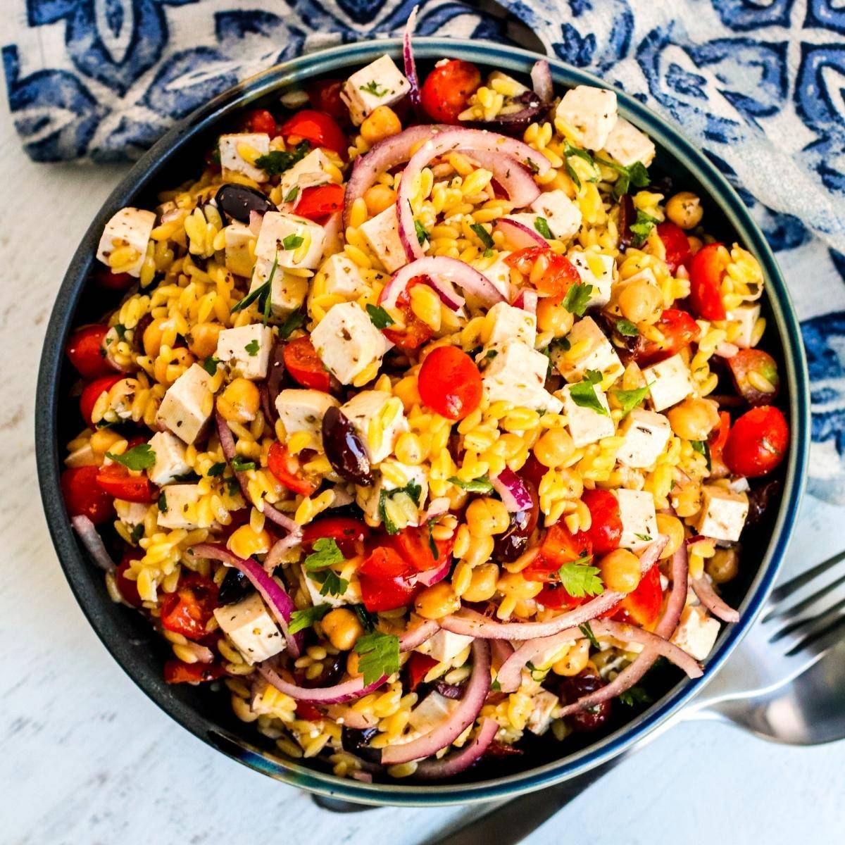 Bowl of vegan Mediterranean orzo salad with chickpeas, vegan feta, tomatoes, red onion, and Kalamata olives.