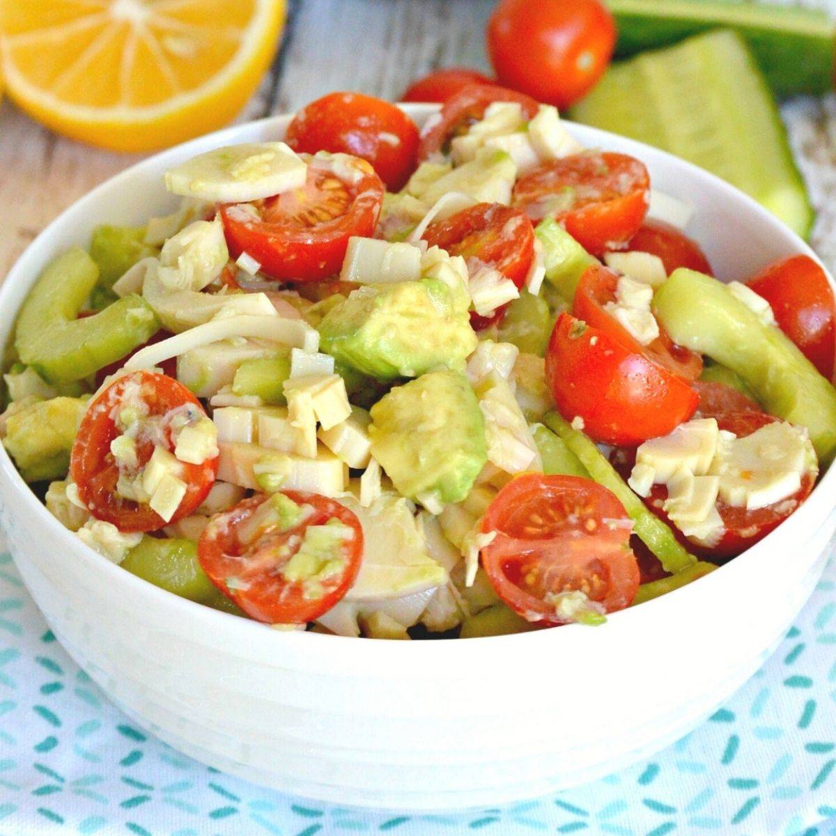 Bowl of salad with hearts of palm, avocado, tomatoes, and cucumbers.