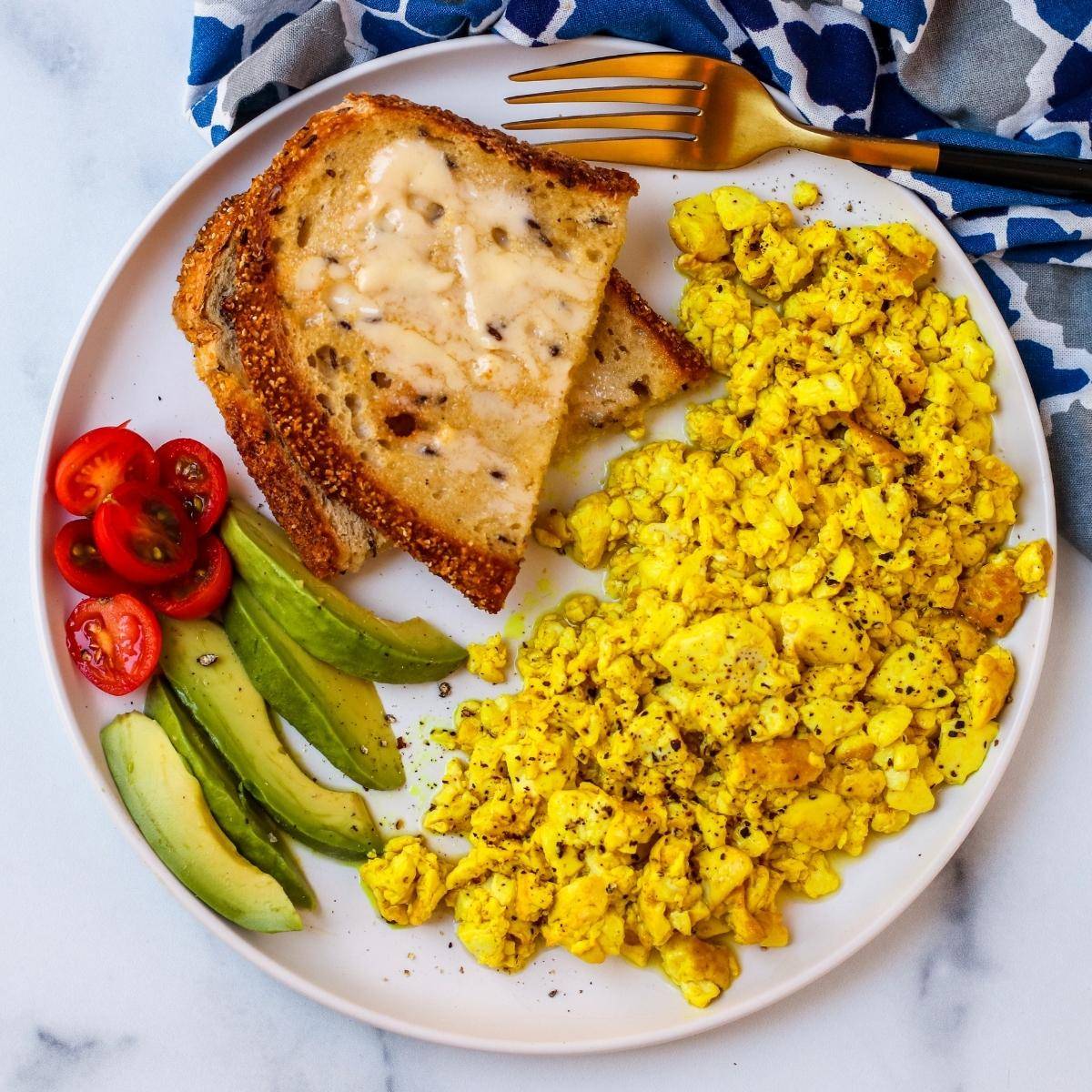 Plate with silken tofu scramble, toast, avocado slices, and cherry tomatoes.