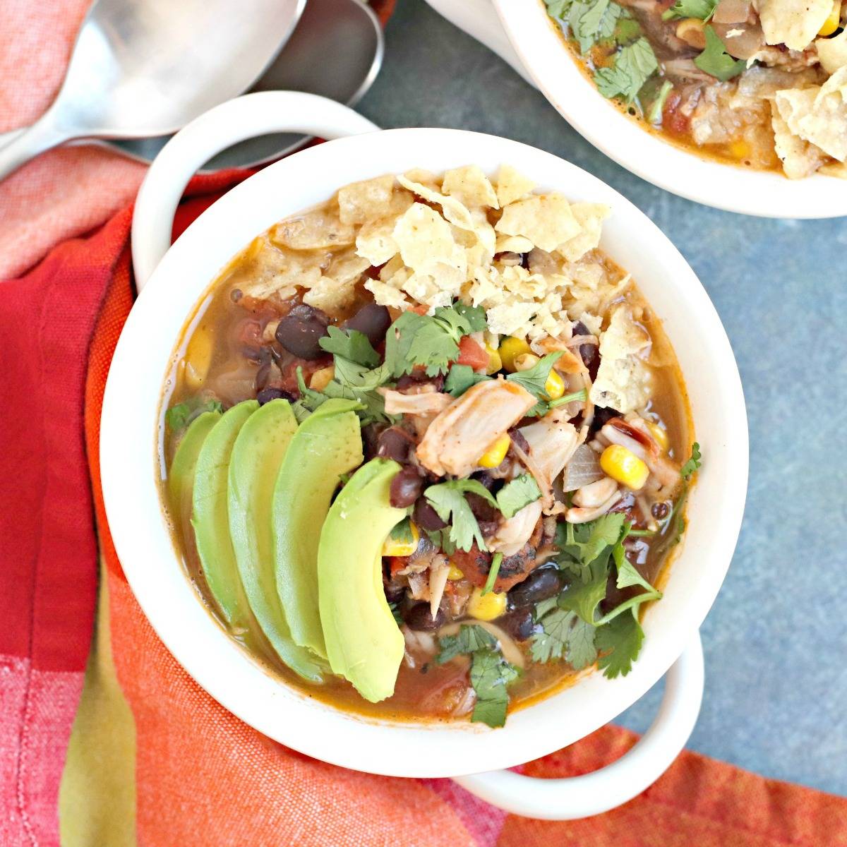 Bowl of jackfruit taco soup topped with crushed tortilla chips, cilantro, and avocado slices.