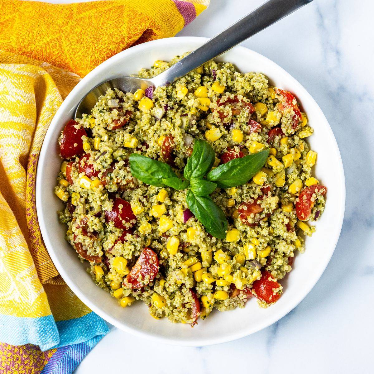 Vegan quinoa salad with corn and tomatoes, garnished with a fresh basil sprig.